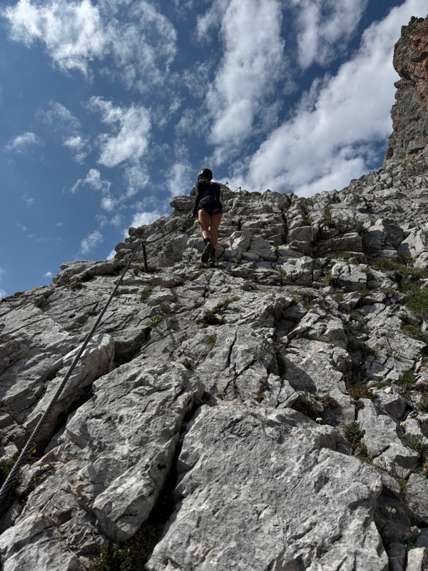 A climber ascending a via ferrata route towards the sky, the cable running alongside