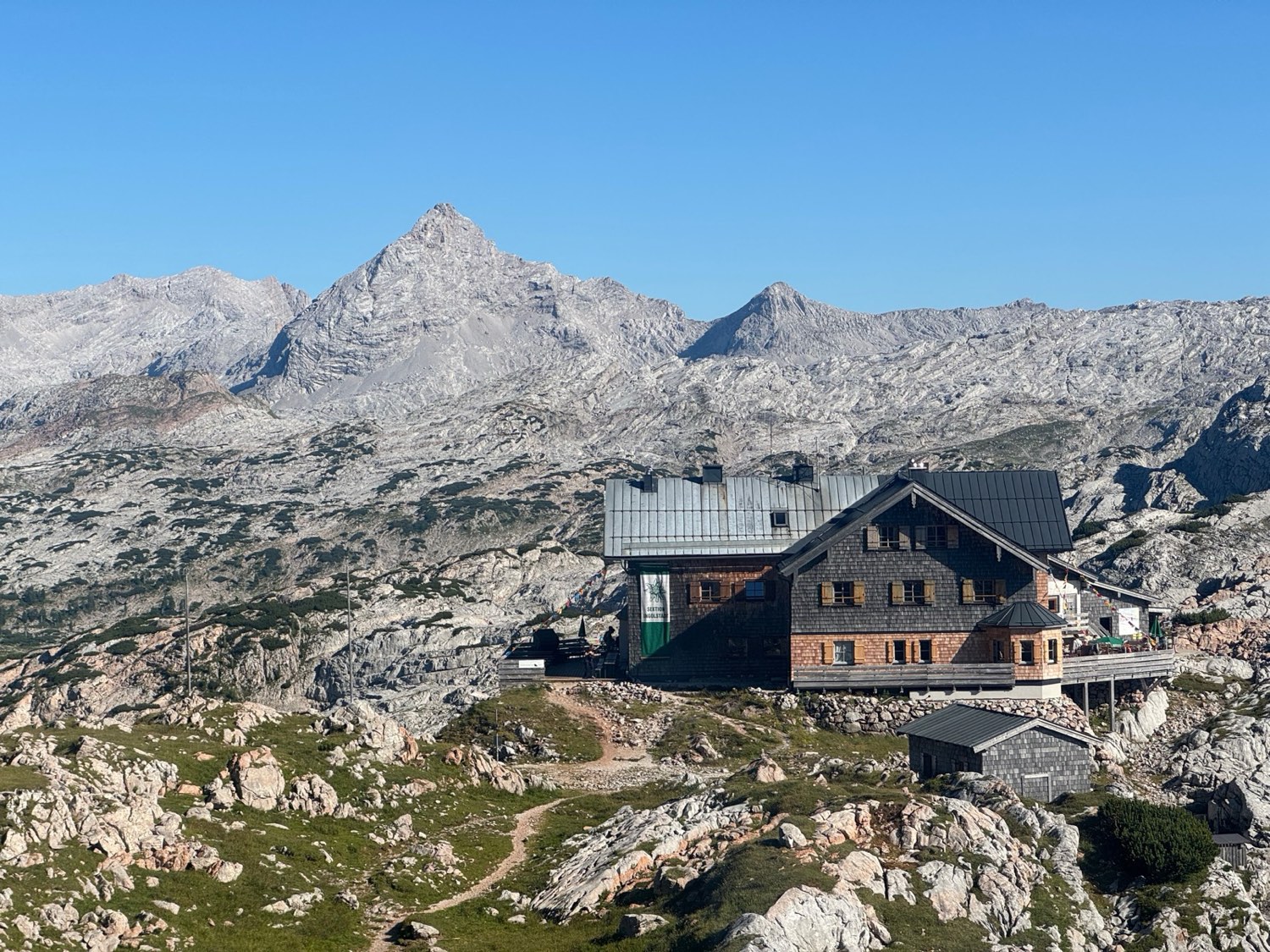 A stone-and-shingle alpine hut on the Steinernes Meer, with a jagged limestone peak rising behind it